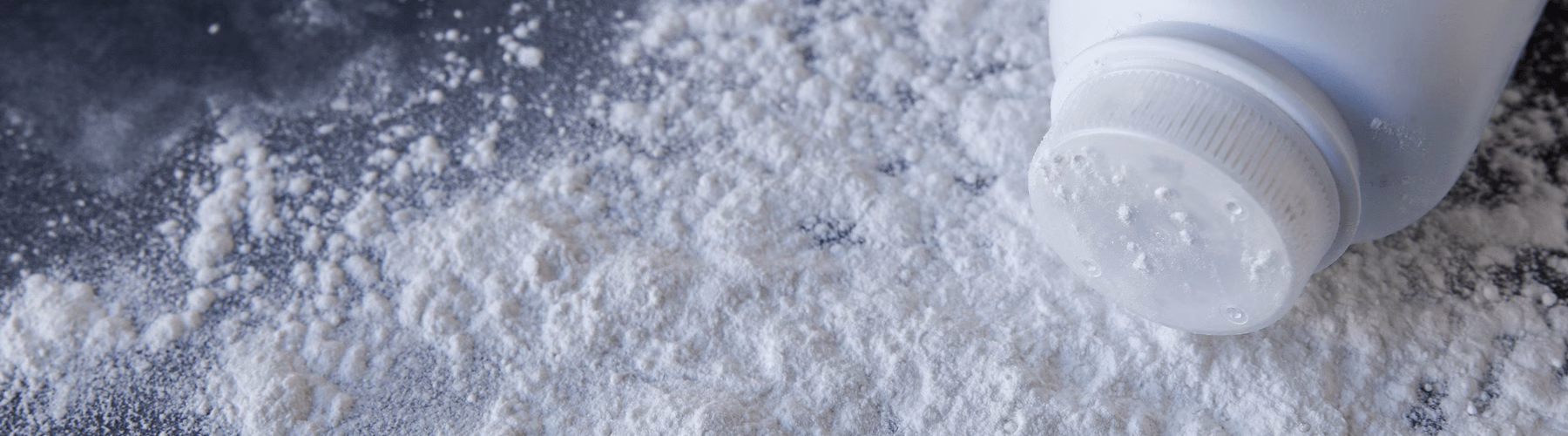 Bottle spilling talcum powder on dark surface